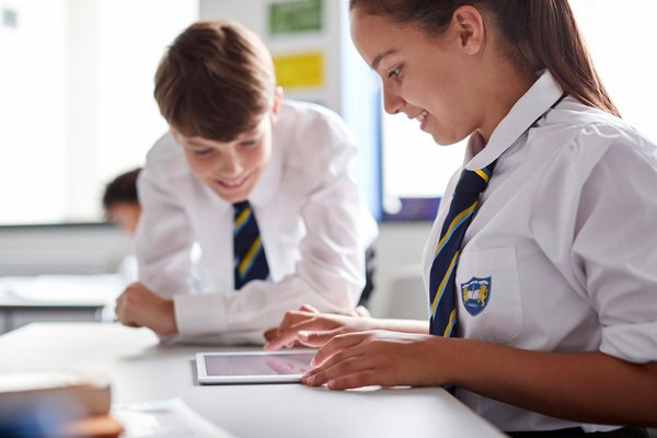 Two High School Students Wearing Uniform Working Together At Desk Using Digital Tablet