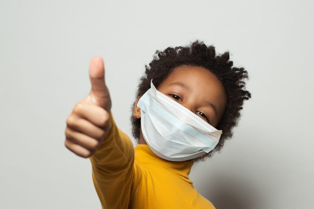 Happy African American black kid in medical protective face mask showing thumb up on white