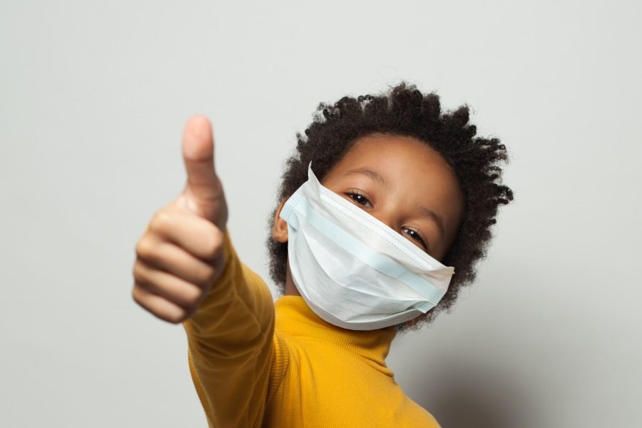 Happy African American black kid in medical protective face mask showing thumb up on white