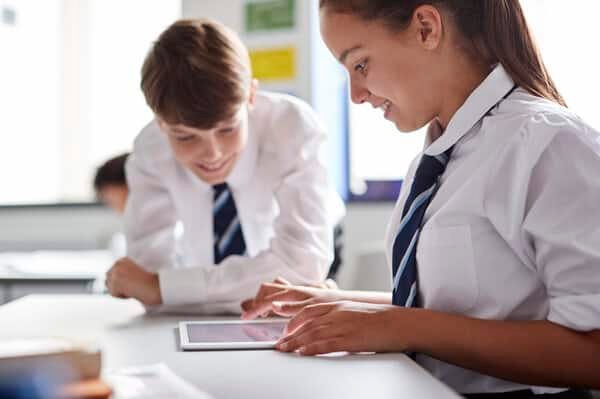 Two High School Students Wearing Uniform Working Together At Desk Using Digital Tablet