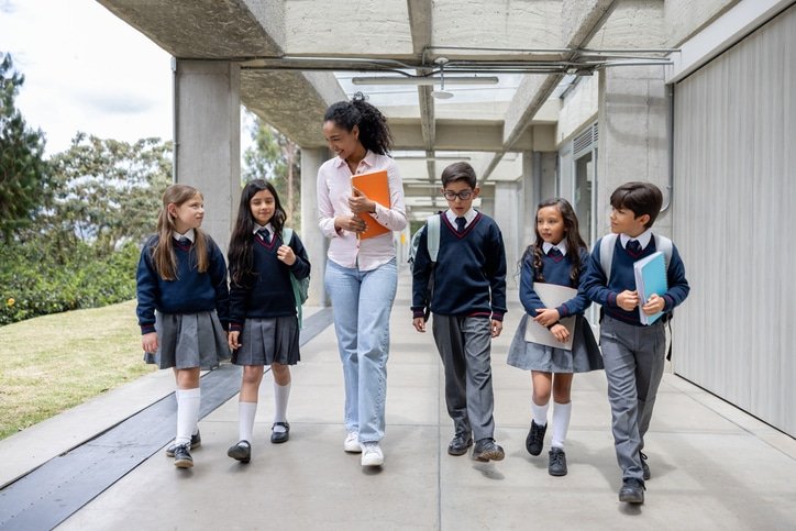 Happy school teacher walking in the corridor with a group of elementary students