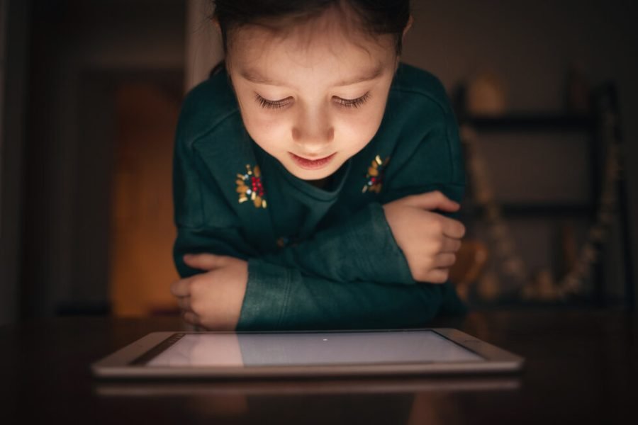 child looks at digital tablet in dark at home at table